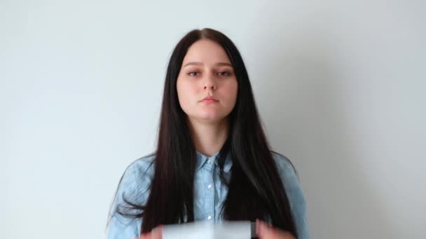 closeup of a young smiling woman girl with long brown hair puts on a medical protective mask, looks at the camera, covid-19 hygiene concept, coronavirus, on a white background, white wall home - Záběry, video