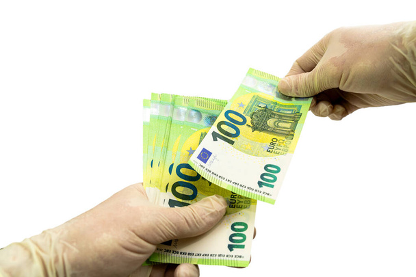 Two hands in white protective gloves hold a bundle of 100 Euro bills. Isolated white background. Virus protection concept. The second hand pulls out a bill. - Photo, image
