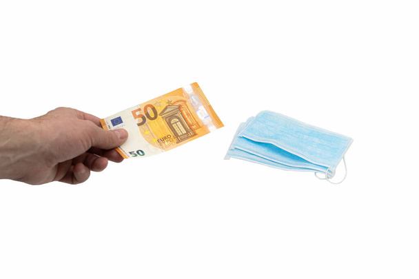 A hand buys a bill of 50 fifty euros in several blue medical surgical masks. The concept of virus protection in Europe. Isolated background - Photo, Image