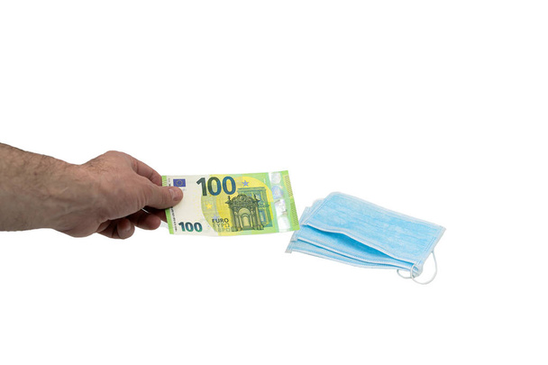 Hand compra un billete de 100 cien euros unas máscaras quirúrgicas médicas azules. El concepto de protección del virus en Europa. Fondo aislado
 - Foto, imagen