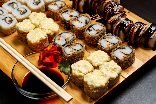 Deliciosos y deliciosos rollos de sushi calientes y fríos sobre la mesa. El sushi diferente - los panecillos con la salsa a la tabla de la cocina japonesa
. - Foto, Imagen