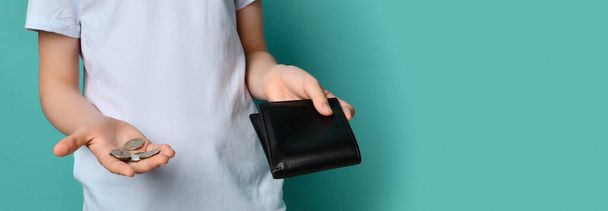 Boy hands hold wallet and showing few coins from black purse in hand over pastel blue. Children fashion economic crisis concept - Photo, image