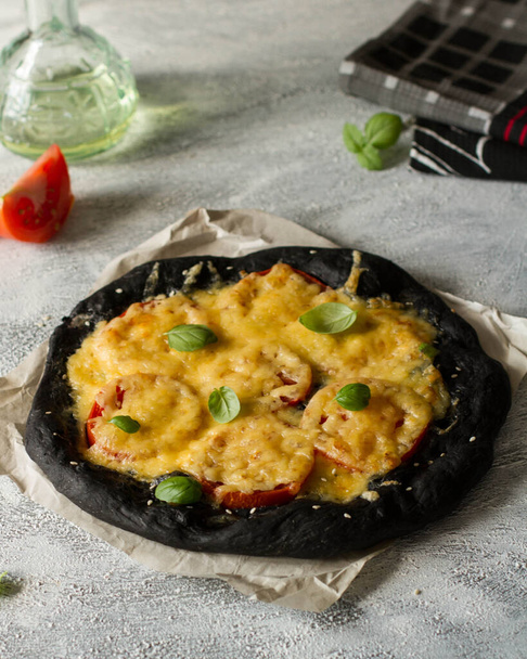 Black dough pizza with tomatoes and cheese. - Φωτογραφία, εικόνα