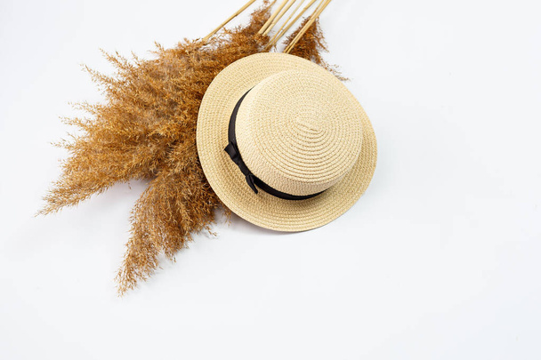 Γυναικείο καλοκαιρινό καπέλο και στεγνό γρασίδι σε λευκό φόντο. Καλοκαιρινές διακοπές, διακοπές, ταξίδια, ταξιδιωτικές ιδέες. Αξεσουάρ παραλίας πάνω όψη. Χώρος για κείμενο. - Φωτογραφία, εικόνα