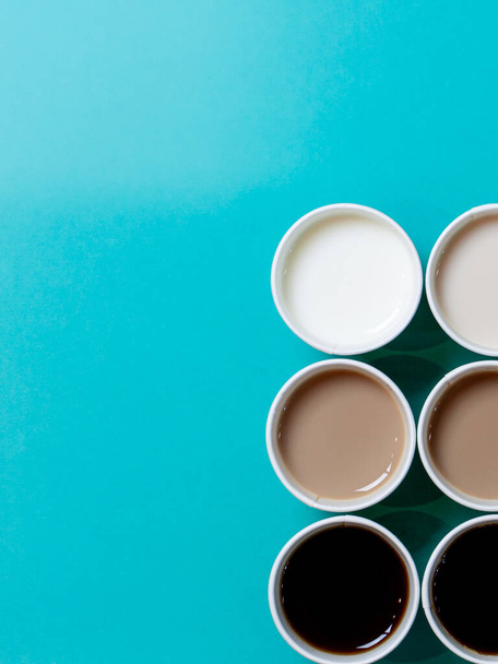 Tazas de café minimalistas dispuestos como para crear un gradiente de color, con diferentes cantidades de leche añadida al café. Fondo turquesa, vista superior plana
 - Foto, Imagen