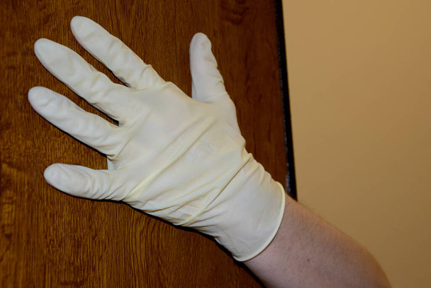 Мужская рука в резиновой перчатке запирает дверь, будучи концепцией остаться дома
. - Фото, изображение