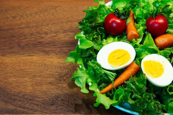 Νόστιμη σαλάτα λαχανικών σε λευκό πιάτο και ξύλινο πιάτο. Πράσινο λαχανικό καρότο ντομάτας και μείγμα αυγών με βαλσάμικο βινεγκρέτ είναι υγιεινό φαγητό - Φωτογραφία, εικόνα