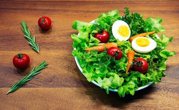 Tasty fresh mix vegetable salad on white dish and wooden plate.  Green vegetable tomato carrot and egg mix with balsamic vinaigrette is healthy food - Photo, Image