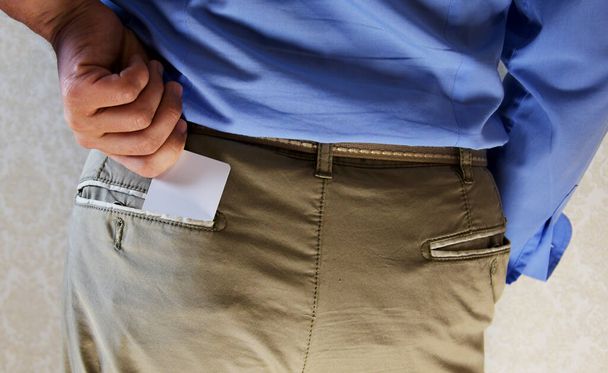 Um jovem de camisa azul e calças leves coloca um cartão eletrônico no bolso de trás de suas calças
. - Foto, Imagem