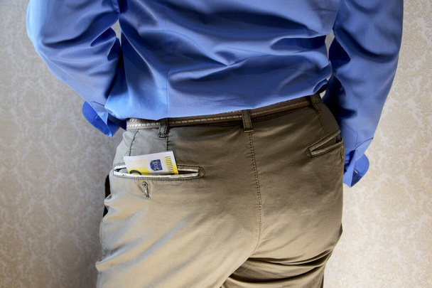 Een jongeman in hemd en broek stopt een paar bankbiljetten, euro in zijn broekzak. - Foto, afbeelding