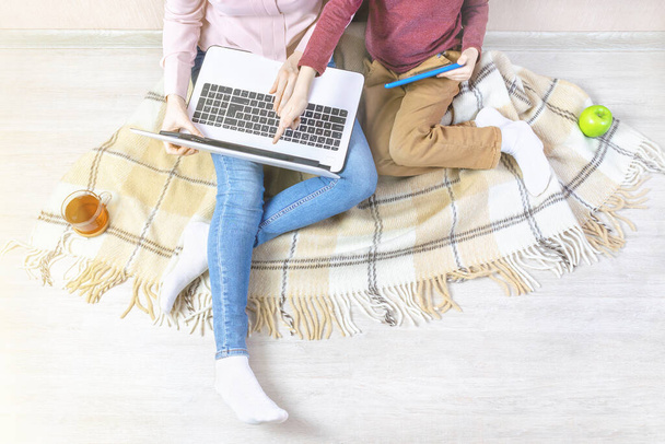 Young woman and boy on the plaid blanket. Mom holds a laptop and shows a hand to her son at the screen, home schooling, distance learning, working from home, remote work, freelance, quarantine. - Photo, image
