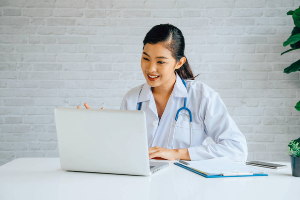 Online video conference chat with Asian female doctor and patient while discussing and diagnosing on laptop and looking at camera - Photo, Image