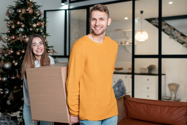 Joyeux jeune adulte famille emménager dans une nouvelle maison ensemble, portant des boîtes en carton, regardant la caméra, debout dans le salon et souriant large
 - Photo, image