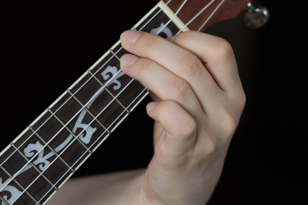 Woman hand playing ukulele on black background - Foto, Imagem