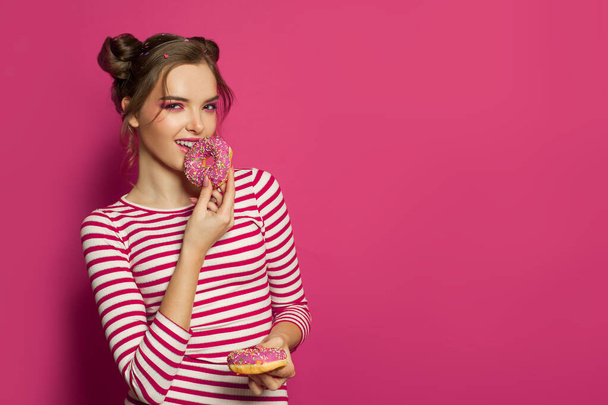 Adorable woman eating donut on vibrant pink background, fashion portrait - Foto, immagini