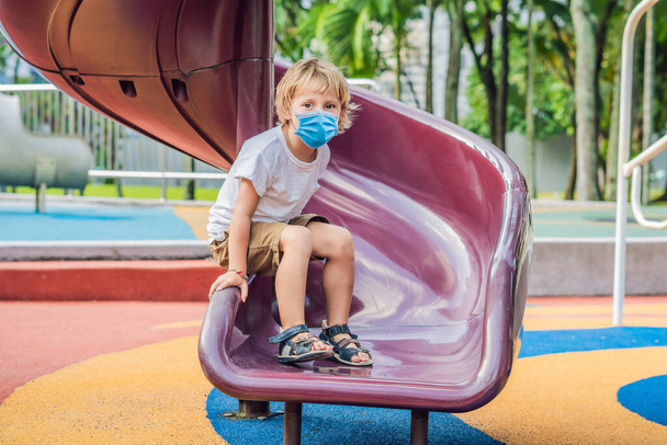 Funny cute happy baby in medical mask playing on the playground. The emotion of happiness, fun, joy Tourists fear the 2019-ncov virus. Medical masked tourists - Photo, image