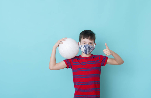 Мальчик в маске из-за коронного вируса играет в мяч на синем фоне. Концепция тренировок онлайн
. - Фото, изображение