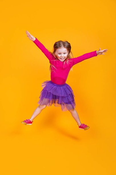 funny little child girl jumping on yellow studio background - Foto, afbeelding