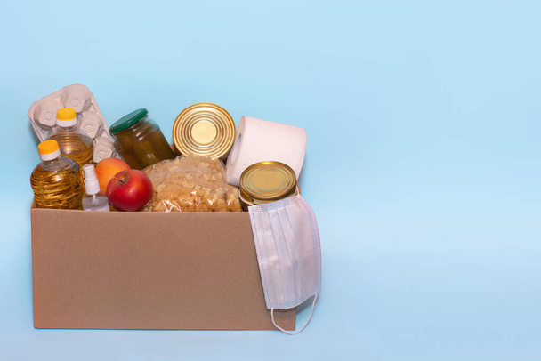 Eten in een kartonnen doos, geïsoleerd op blauwe achtergrond, kopieerruimte. Coronavirus Relief Funds and Donations.Charity donaties. Donaties aan de Voedselbank - Foto, afbeelding