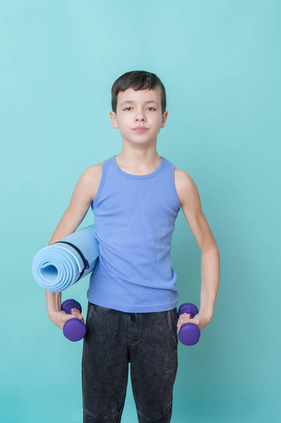 Portrait of a handsome teenage sport boy with dumbbells  and gym mat. Workout online concept. - Fotoğraf, Görsel