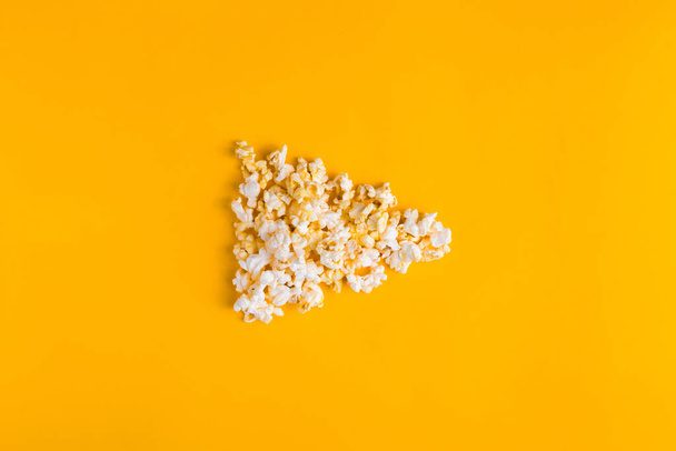 Popcorn in the shape of play button on yellow background. Flat lay banner, top view. To go to the cinema. I like watching films. - Photo, Image