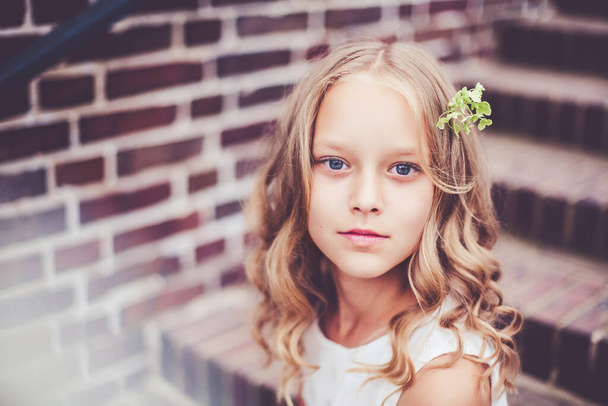 Lähikuva muotokuva kaunis 9-10 vuotias tyttö vaaleat kiharat hiukset istuu portaissa
. - Valokuva, kuva