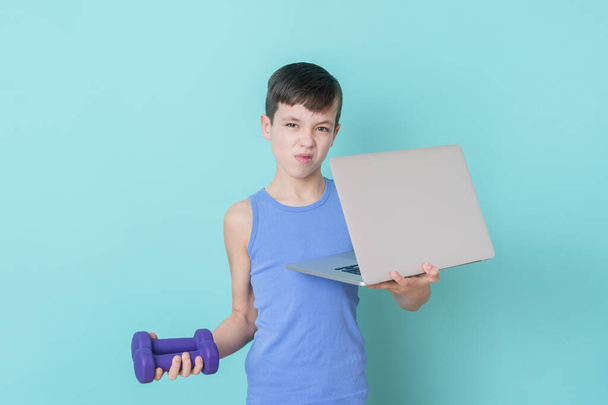 Boy watching online video on laptop and doing fitness exercises at home. Workout online concept. - Foto, imagen