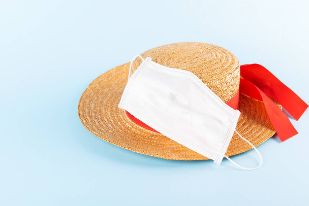 Un sombrero de paja lleva una máscara médica protectora sobre un fondo azul pastel. Vacaciones de verano Coronavirus, Covid-19 y concepto de viaje. Protección de la salud durante el viaje
 - Foto, Imagen