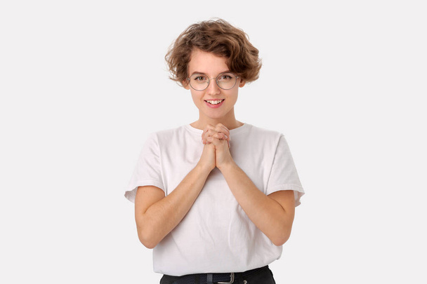 Fröhlich lächelndes Mädchen in weißem Hemd und Brille mit kurzem Haar hält Hände in Namaste oder Gebetsgeste zusammen und bedankt sich isoliert vor weißem Hintergrund für Hilfe - Foto, Bild