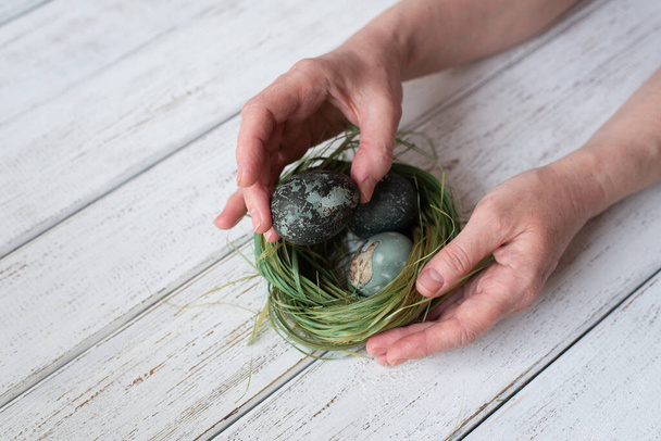 Man holding painted eggs for easter. nest of grass. white wooden table - Foto, imagen
