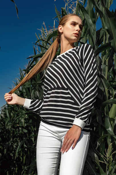 Retrato de una chica de pelo rubio con ropa elegante y de moda, entre el follaje de un campo de maíz
. - Foto, imagen