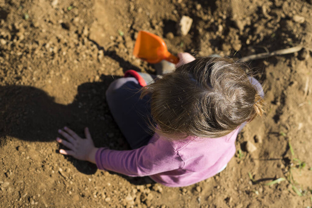 Little child girl digging soil with a scoop in the garden during covid-19 pandemic  lockdown. Outdoor activity idea for children during home staying. Top view, aerial point of view. - Photo, Image