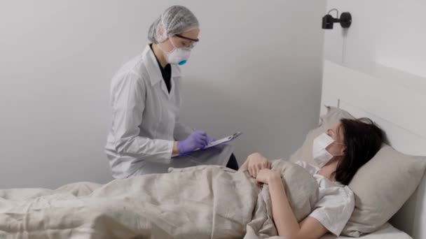 ιολόγος γιατρός ζητά από γυναίκα ασθενή με άγνωστη ασθένεια στο δωμάτιο του νοσοκομείου, συμπληρώνοντας χαρτί - Πλάνα, βίντεο