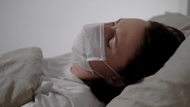 mulher doente com máscara médica está tossindo dificilmente deitado na cama no quarto do hospital, close-up da cara
 - Filmagem, Vídeo