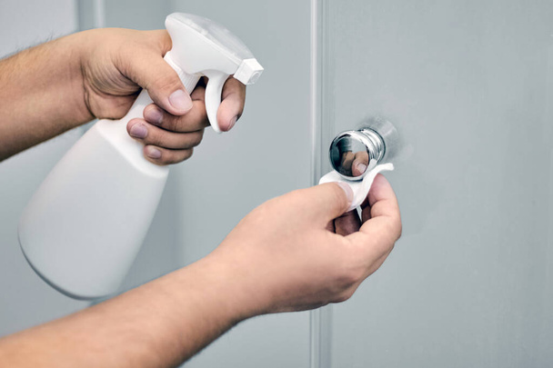 A person treats door handles with an alcohol-containing substance using a spray and a cotton pad. Prevention and hygiene of covid-19 virus infection - Valokuva, kuva