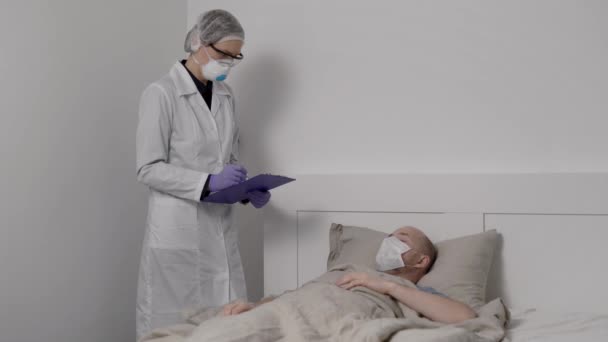 wirusolog pyta chorego pacjenta płci męskiej z twardą postacią wirusa grypy w pokoju szpitalnym, epidemią zakażeń układu oddechowego - Materiał filmowy, wideo