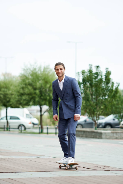 Attractive bearded young man in classic suit on skateboard. Eleg - Foto, imagen