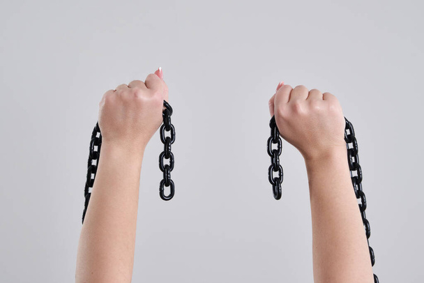 Female hands holding a broken metal chain over grey background with copy space - Foto, Imagen