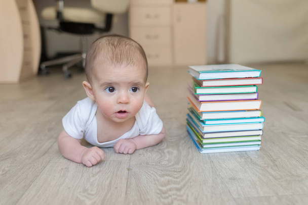 Pasgeboren baby met boeken. Een jongetje in witte kleren en blauw. Mooi portret van een peuter. Grote ogen baby. Afstandsonderwijs. Afstandsonderwijs - Foto, afbeelding