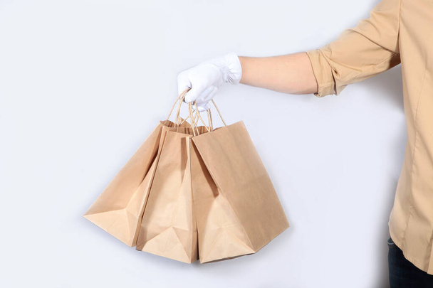 A man in a uniform and white gloves is holding a paper shopping bag. Unrecognizable photo. The concept of service delivery. Advertising space. Copy of the space. - Foto, imagen