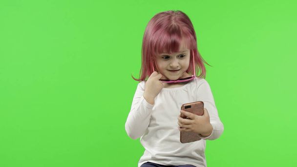 Tyttö käyttää älypuhelinta. Lapsi emotionaalisesti puhuu matkapuhelimeen, ota selfie
 - Valokuva, kuva