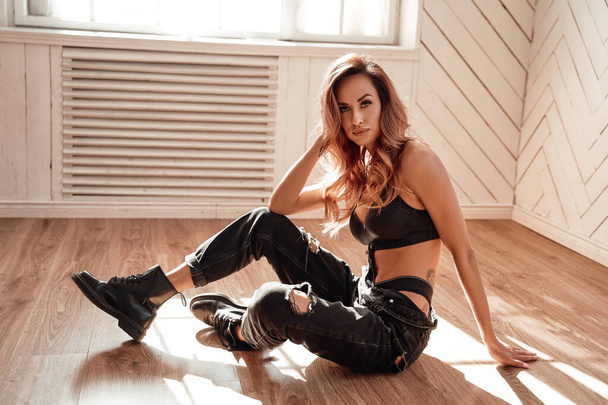 Ritratto di una giovane e bella donna in lingerie nera sportiva e jeans appoggiati su un pavimento di legno, mentre cerca premuroso e calmo
 - Foto, immagini