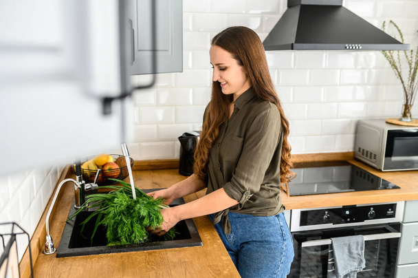 A woman with a bunch of dill in hands in kitchen - Photo, image