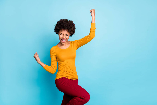 Portrait of crazy delighted afro american girl celebrate lottery victory feel lucky raise fists scream yeah wear red pants isolated over blue color background - Photo, Image
