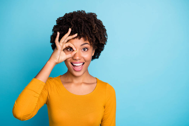 Portrait of excited astonished afro american girl show okay sign make binoculars watch look impressed scream wow omg wear stylish trendy sweater isolated over blue color background - Fotó, kép