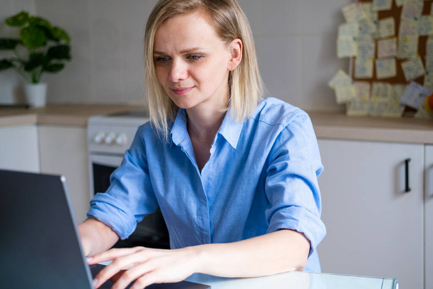 Blonde Woman is working office work remotely from home on kitchen. Using computer. Distance learning online education and work. - Foto, Imagem