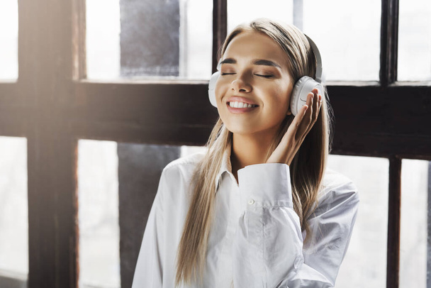 Молодая женщина слушает музыку в наушниках. Потоковое аудио и обмен информацией в социальных сетях, интернет-аккаунтах
. - Фото, изображение