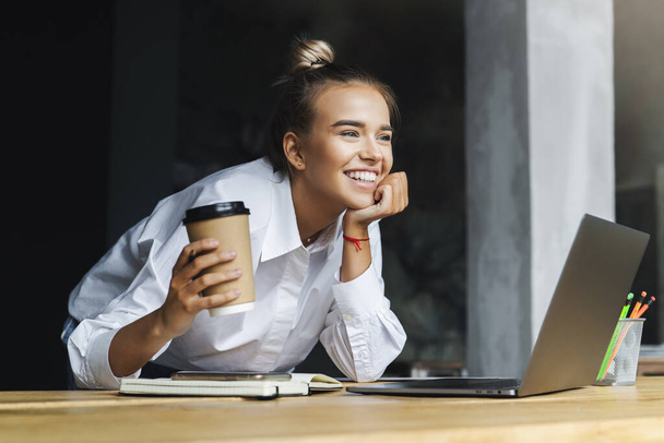 Beautiful young business woman working remotely from home. Smiling woman sits in front of laptop - Foto, immagini