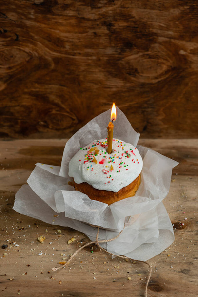 Easter cake with a burning candle in parchment paper on a wooden background - Foto, imagen
