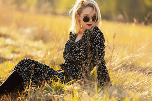 Blonde girl is sitting at countryside in sunset time - Photo, Image
